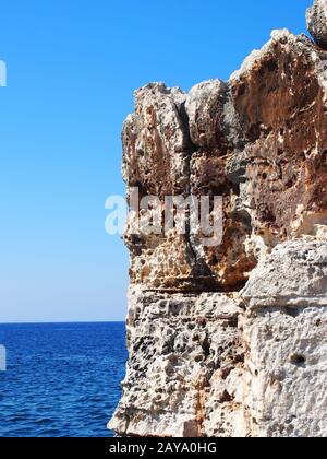 uno sperone roccioso frastagliato ruvido contro un cielo e un mare luminosi e azzurri Foto Stock