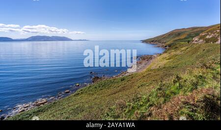 Linea rocciosa costale e montagne a distanza con cielo e mare blu Foto Stock