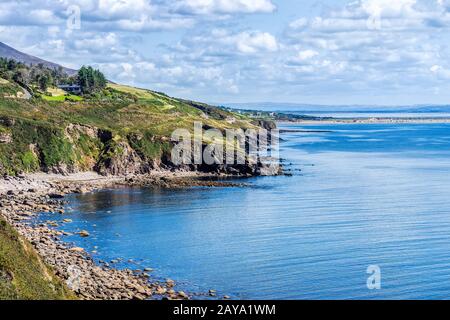 Linea rocciosa costale e montagne a distanza con cielo e mare blu Foto Stock