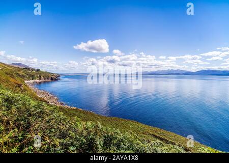 Linea rocciosa costale e montagne a distanza con cielo e mare blu Foto Stock