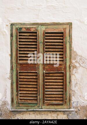 antica finestra verde chiuso dipinta persiane marrone in una parete bianca con cracking cemento e intonaco Foto Stock