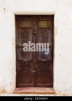 vecchie porte doppie in legno marrone con vernice sfaldabile sbiadita e maniglie arrugginite lucchettate chiuse Foto Stock