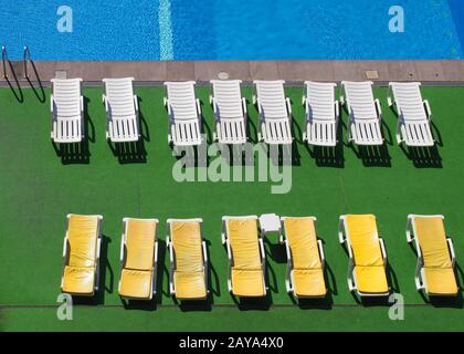 vista aerea dei lettini su uno sfondo verde accanto ad una piscina blu sotto la luce del sole Foto Stock