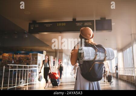 Trasporto pubblico a tema. Giovane donna in piedi con schiena in abito e cappello dietro zaino e attrezzature da campeggio per il sonno Foto Stock