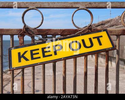 giallo tenere fuori segno su un metallo arrugginito chiuso attraverso una strada che conduce al mare Foto Stock