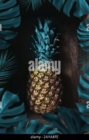 Ananas fresco su un vecchio sfondo di legno decorato con una cornice di foglie di palma. La frutta tropicale Foto Stock