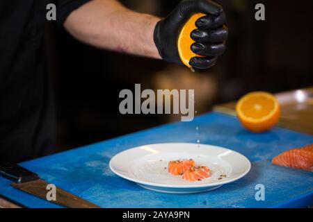 La cucina a tema è una professione di cucina. Primo piano della mano di un uomo caucasico in una cucina del ristorante che prepara filetti di pesce rosso Foto Stock