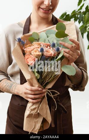 Ragazza fiorista con bouquet creativo da fiori freschi rose in una carta su uno sfondo chiaro. Primo piano. Congratulazioni Foto Stock