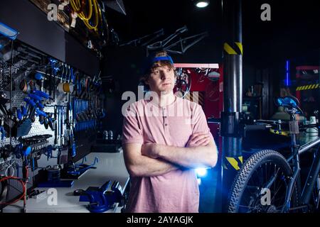 Servizio di trasporto per piccole imprese e biciclette. Ritratto di un giovane in un cappello che si posa sullo sfondo di un laboratorio di biciclette Foto Stock