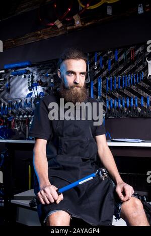 Ritratto di piccola impresa proprietario di giovane uomo con barba. Ragazzo di bicicletta meccanico officina lavoratore seduto con l'attrezzo in mano Foto Stock