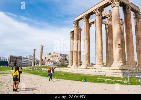 Turisti fotografati di fronte al Tempio Greco di Zeus Olimpio con l'Acropoli di Atene sullo sfondo Foto Stock