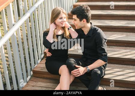 Bella giovane coppia multirazziale, coppia studentesca innamorata, sedersi scala in legno in città. Bel bruna turco ragazzo abbraccio Foto Stock