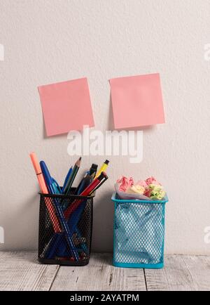 Luogo di lavoro con due note rosa bastone vuoto Pad mettere su parete bianca appeso sopra due matita completa Pot su scrivania riempito di penne Foto Stock