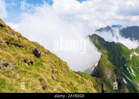 grande scenario estivo di alta catena montuosa. ripidi pendii con rocce, erba e macchie di neve. nuvole sul cielo blu. esplora il crinale di fagaras di romani Foto Stock