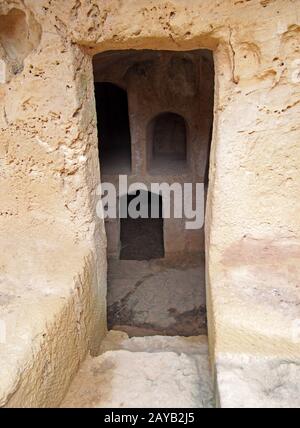 una porta stretta scavata nella roccia con gradini che conducono a camere sotterranee scure presso le tombe dei re di paphos cipro Foto Stock