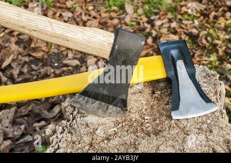 A due assi con lame in acciaio bloccati nel vecchio ceppo in autunno foglie secche sfondo Foto Stock