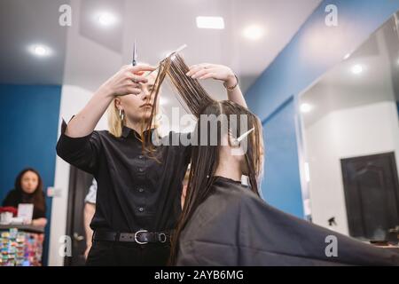 parrucchiere che tiene forbici e pettine e fa cliente donna taglio di capelli. Giovane bella donna capelli tagliati in salone di bellezza. Processo di Foto Stock