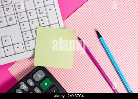 Foglio di appunti appiccicato sulla tastiera del computer vicino a un tessuto a motivi geometrici e fisso sopra un tavolo colorato. Strumento di elaborazione dati mac Foto Stock