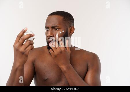 Sorridente uomo afro applicare la crema sul suo volto. L'uomo la cute del concetto di cura Foto Stock