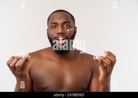 Sorridente uomo afro applicare la crema sul suo volto. L'uomo la cute del concetto di cura Foto Stock