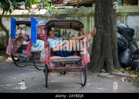 Street scene con un driver risciò dormiente a Yogyakarta, Java, Indonesia. Foto Stock