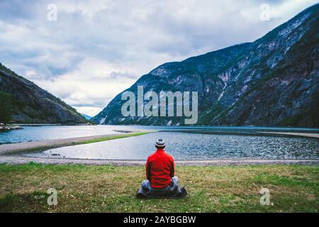 Uomo che fa yoga meditazione sui tappetini nella mattina nuvolosa spazi aperti vicino al bellissimo lago Norvegia. Meditazione Yoga in montagna uomo trave Foto Stock