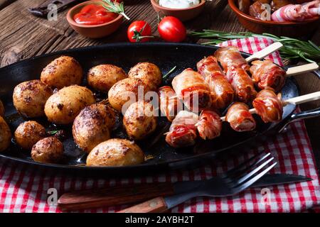 Datteri rustici avvolti in pancetta e patate giovani arrostite. Foto Stock