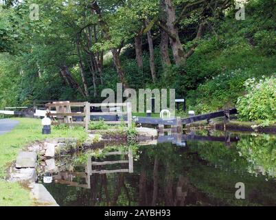 vecchie porte di legno con alberi e fiori riflessi in acqua con posti di ormeggio e recinzioni sul canale rochdale in rawde Foto Stock