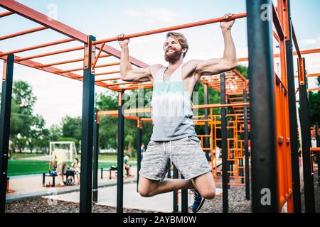 atleta forte che fa pull-up su barra orizzontale. Uomo muscoloso che fa tirare su barra orizzontale in parcheggio. Palestra Durante Il Lavoro Foto Stock