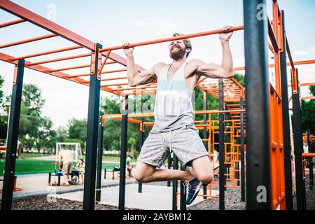 atleta forte che fa pull-up su barra orizzontale. Uomo muscoloso che fa tirare su barra orizzontale in parcheggio. Palestra Durante Il Lavoro Foto Stock