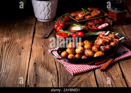 Datteri rustici avvolti in pancetta e patate giovani arrostite. Foto Stock