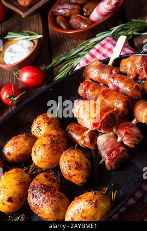 Datteri rustici avvolti in pancetta e patate giovani arrostite. Foto Stock