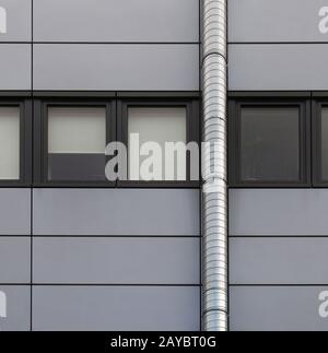 pannelli di rivestimento grigi su un edificio industriale con una fila di telai posteriori e un tubo d'argento che corre sulla parete Foto Stock