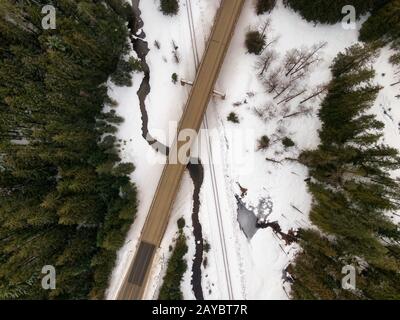 Veduta aerea Dall'Alto di un'autostrada che attraversa il fiume e i binari ferroviari durante l'inverno. Preso nell'interno della Columbia Britannica, Canada. Foto Stock