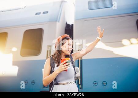 zaino viaggiatore donna che sventola mano alla stazione ferroviaria piattaforma estate vacanza concetto di viaggio. Saluto turistico femminile e enjo Foto Stock