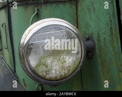 primo piano del faro di un vecchio camion abbandonato con griglia e pannelli verdi arrugginiti Foto Stock