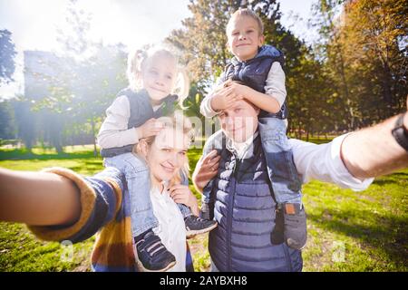 Bella giovane coppia prendere selfie foto autoritratto portando figlio e figlia sulle spalle ponendo sorriso felice. Punto Di Vista Shot Foto Stock