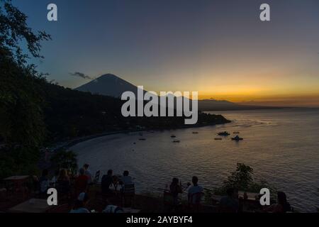 La gente guarda il tramonto dietro il Monte Agung (un vulcano attivo) dal punto di tramonto Amed a Bali Est, Indonesia. Foto Stock