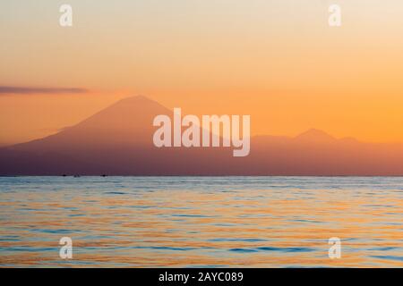 Vista dall'Isola di Lombok dei due vulcani attivi, il Monte Agung (a sinistra) e il Monte Batur a Bali, Indonesia, al tramonto. Foto Stock