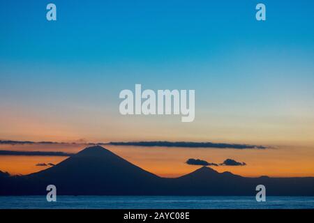 Vista dall'Isola di Lombok dei due vulcani attivi, il Monte Agung (a sinistra) e il Monte Batur a Bali, Indonesia, al tramonto. Foto Stock