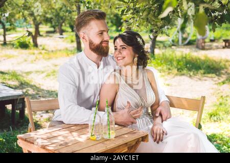 Coppia attraente sposi novelli, momento felice e gioioso. Sposa e sposo sedersi al tavolo set per due in legno. Concetto romantico data. Foto Stock