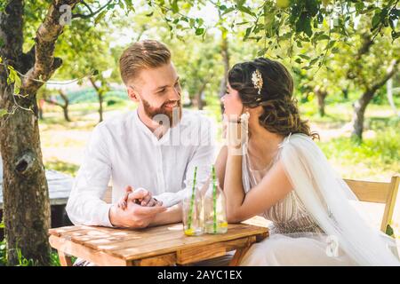 Coppia attraente sposi novelli, momento felice e gioioso. Sposa e sposo sedersi al tavolo set per due in legno. Concetto romantico data. Foto Stock