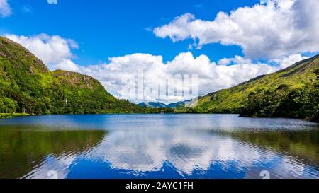 Fotografia di lago e montagna con nuvole puffy riflesso in acqua. Connemara, Irlanda Foto Stock