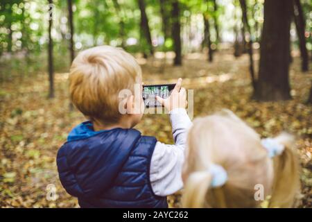 Bambini bambini preschoolers fratello e sorella caucasico fare le foto l'un l'altro sulla macchina fotografica del telefono mobile nel parco di foresta autunno. Il Foto Stock