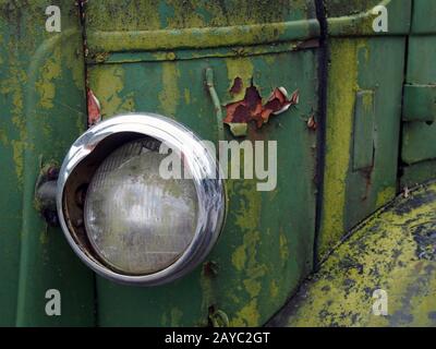 primo piano del faro di un vecchio camion abbandonato con griglia e pannelli verdi arrugginiti Foto Stock