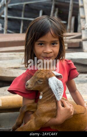 Scena del villaggio con una ragazza che tiene una capra del bambino nel villaggio di Sangean, Isola del Vulcano Dell'Api di Sangeang vicino all'isola di Sumbawa, Isole di Sunda minori, Indonesia. Foto Stock