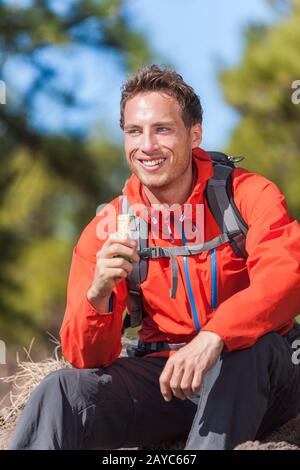 Uomo escursionista sano stile di vita all'aperto mangiare bar muesli durante l'escursione in montagna. Happy People mangiare granola cereali bar snack vivere uno stile di vita attivo in natura. Foto Stock