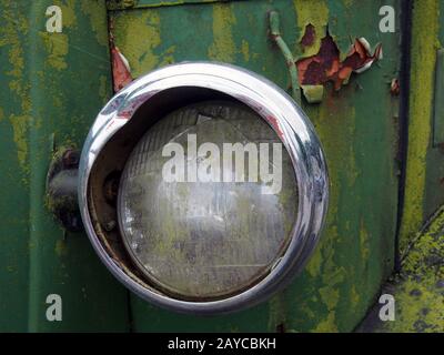 primo piano del faro rotto di un vecchio camion abbandonato con vernice verde arrugginita Foto Stock