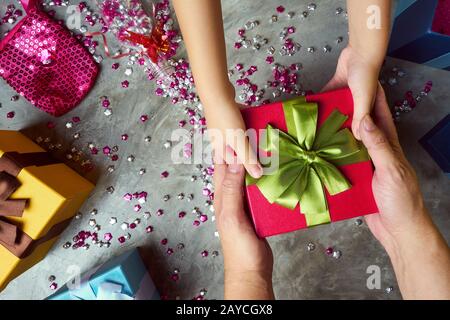 Chiudi le mani del genitore che dà un regalo di Natale al bambino con la scatola colorata del regalo e lo sfondo piccolo del mestiere della stella. Cementa testo Foto Stock