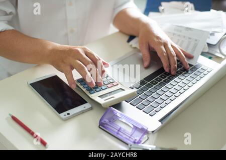 Gli uomini d' affari lavorare con la calcolatrice e il computer portatile sul tavolo bianco in ufficio Foto Stock